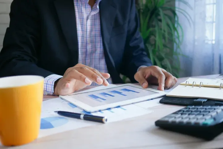 Dirigeant de PME analysant des graphiques de coûts sur une tablette, calculatrice à côté