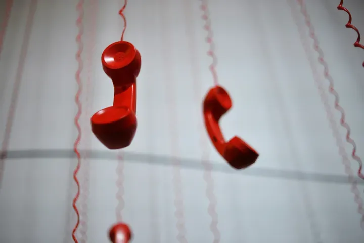 Combinés téléphoniques rouges suspendus à des fils, image du réflexe d'appeler le dépannage